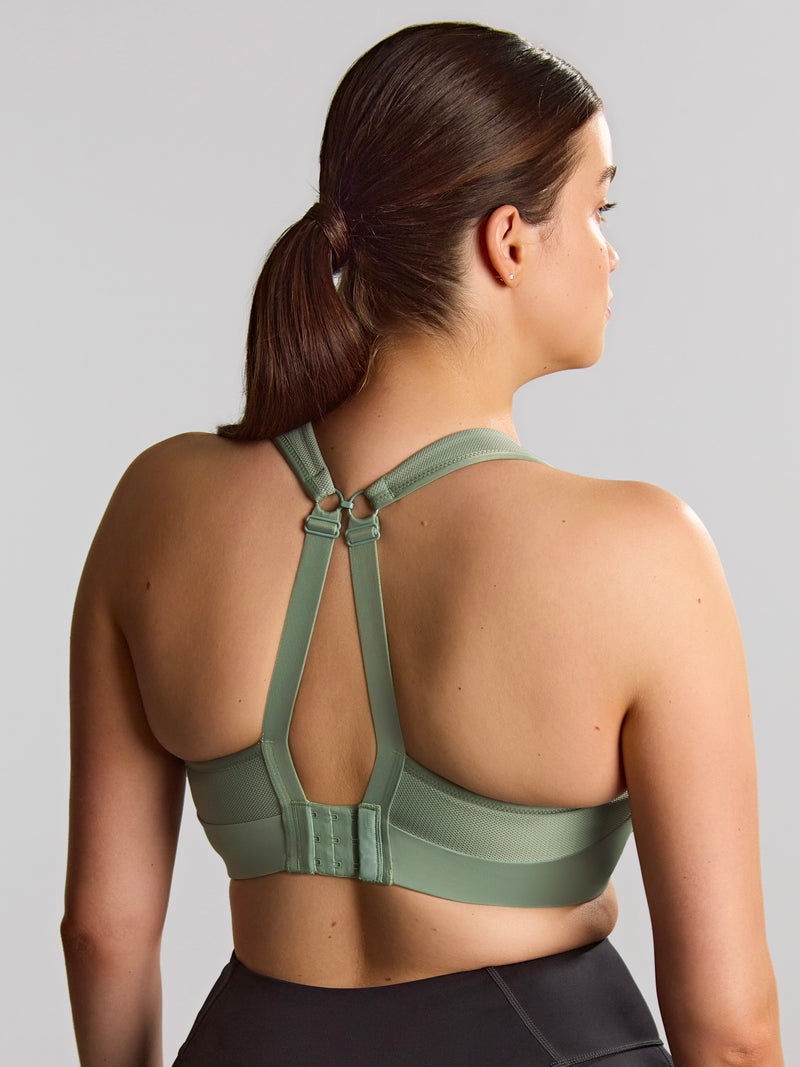 Woman wearing a green sports bra and black leggings on a gray background