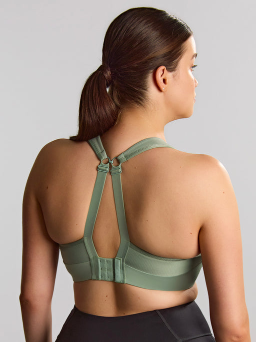 Woman wearing a green sports bra and black leggings on a gray background